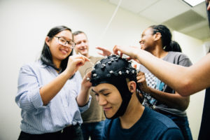 students working in lab with subject wearing cap for experiment